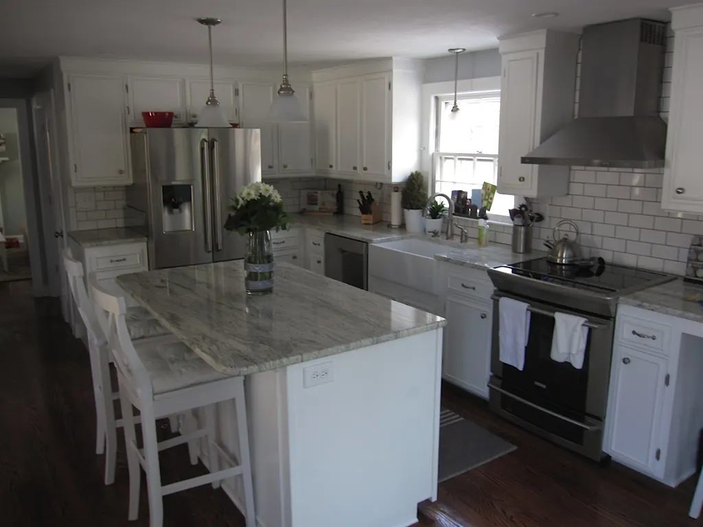 White kitchen with granite island, subway tile backsplash and stainless range hood