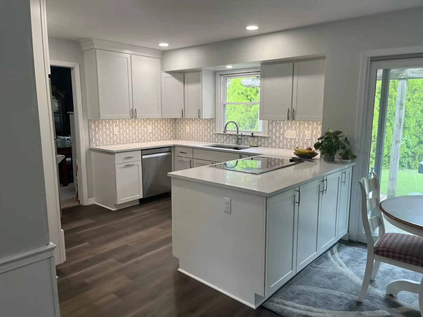 White shaker kitchen with island, tiled backsplash and dark wood-look floor