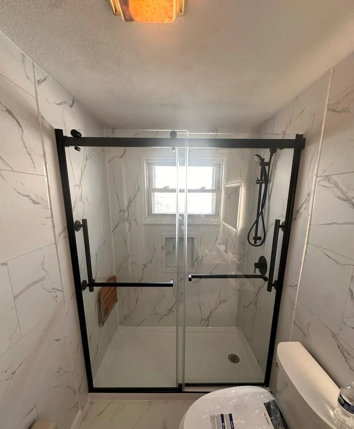 Walk-in shower with marble-look walls and black-framed sliding glass doors